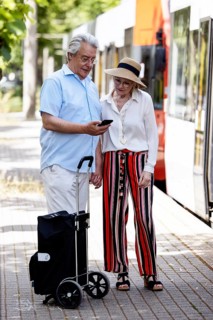 Elderly couple waiting for the tram at a stop with a smartphone in hand