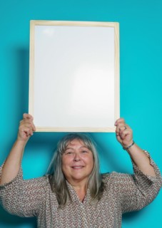 Older white-haired woman holding a white board to paste text on