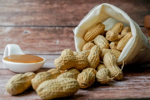 Shelled peanuts in a cloth bag and spoon with peanut butter on a wooden table