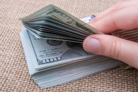 Hand holding banknote bundle of US dollar on a linen canvas background