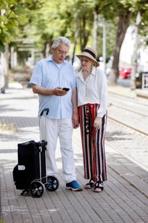 Elderly couple waiting for the tram at a stop with a smartphone in hand