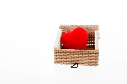 Red heart shaped object placed in a straw box on white background