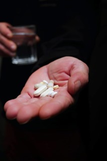 Person in semi-darkness with pills in one hand and a glass of water in the other black background and copy space