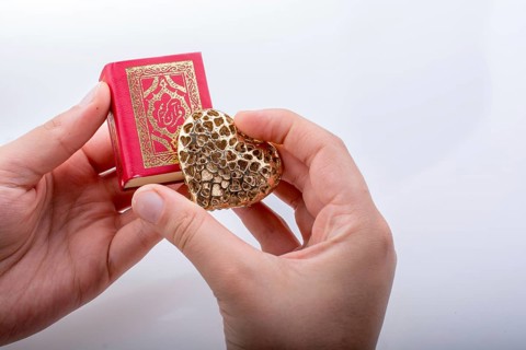 Hand holding Heart shape and Islamic Holy Book Quran