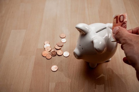 Male hand puts 10 euro note into piggy bank