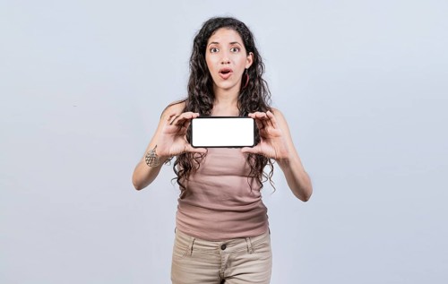 Surprised girl showing blank screen of smart phone. Latin girl showing horizontal screen of cell phone