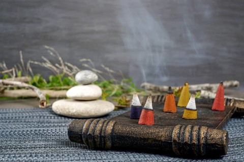Colorful incense cones burning and smoking on a wooden tray with stacked zen stones
