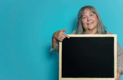 Older white-haired woman holding a blackboard with space for copying text