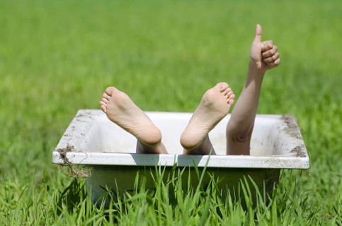 Woman Lying in a Bathtub on a Green Field and Showing OK Signal with Her Hand