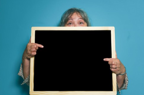 Older white-haired woman holding a blackboard with space for copying text