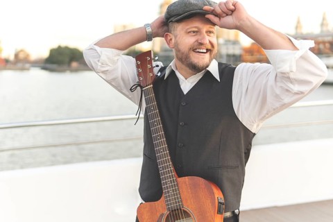 Guitarist posing on a bridge over a river with his guitar