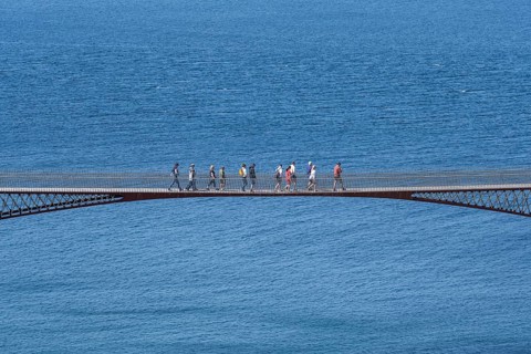 Tourists walk across the new footbridge to the peninsula with the castle ruins of Tintagel Castle