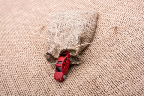 Red toy car coming out of a linen sack on a linen canvas