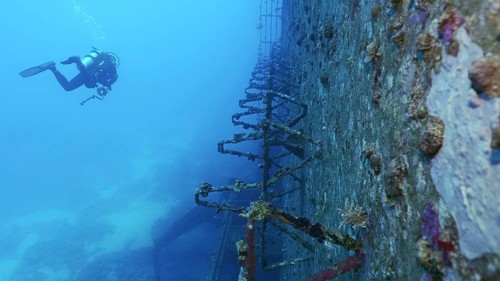 Scuba diver swim along deck of ferry Salem Express shipwreck approaching the ship's superstructure