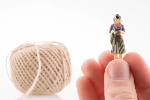Woman figure beside a linen spool of thread on a white background