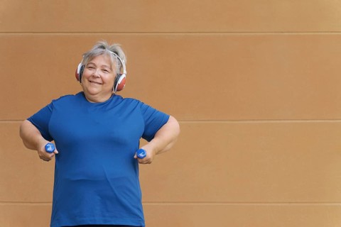 White haired obese older woman exercising with dumbbells and headphones listening to music for weight loss .isolated on orange background and copy space