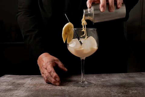 Waitress dressed in black serving a banana cocktail with ice and a slice of banana with a cocktail shaker