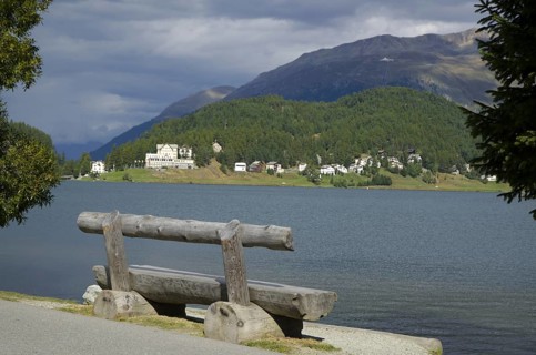 Wood Bench and Trees on St Moritz Lake with Mountain and Grey Clouds in a Sunny Day in Switzerland