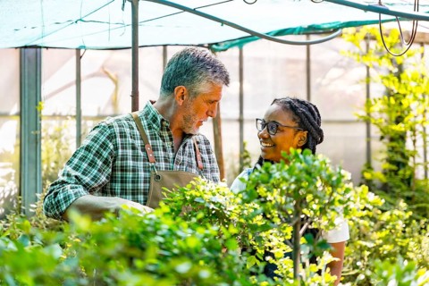 Master gardener teaching flower nursery student girl checking plants in greenhouse