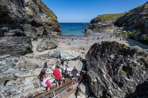 Tourists descend between rock cliffs on a staircase to Tintagel Haven