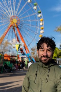 Portrait of latino man in an amusement park posing happy with the ferris wheel in the background