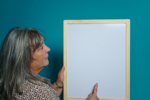 Older white-haired woman holding a white board to paste text on