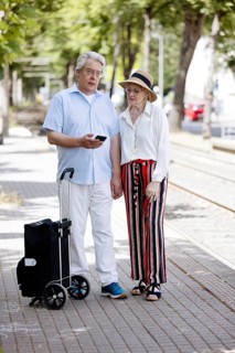 Elderly couple waiting for the tram at a stop with a smartphone in hand