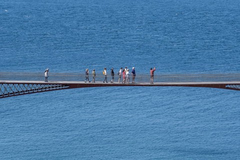 Tourists walk across the new footbridge to the peninsula with the castle ruins of Tintagel Castle