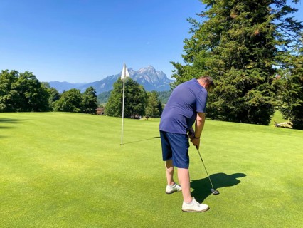 Golfer on Putting Green with Mountain and the Moon View in a Sunny Summer Day in Burgenstock