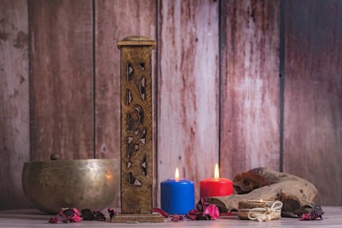 Wooden incense burner with colored candles and Tibetan bowl on a wooden background