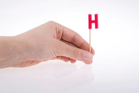 Color candle in hand on sticks writes the letter H