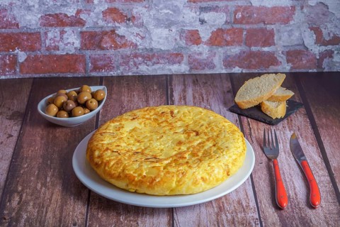Typical spanish potato omelette freshly made on a wooden table with cutlery