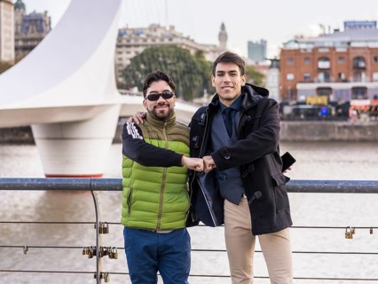Two male friends hugging while looking at camera near Puente de la Mujer