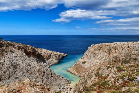 Beautiful view of z-shaped cove or lagoon in typical hills of Crete landscape. Clear blue sky and beautiful clouds on sunny day. Azure sea waters. Stefanou beach