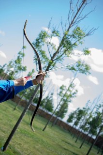 Archer with bow in traditional clothes shooting an arrow