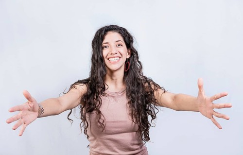 Happy young latin woman welcoming with open arms isolated. Hospitable girl opening arms to the camera. Smiling girl asking for a hug