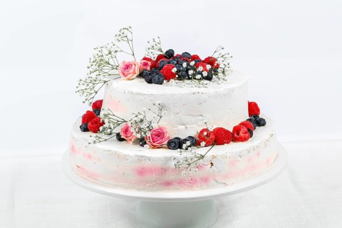 Summery fresh two tier wedding cake decorated with berries and flowers festive cream cake on light background