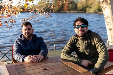 Two friends sitting at an outdoor bar on a river at sunset