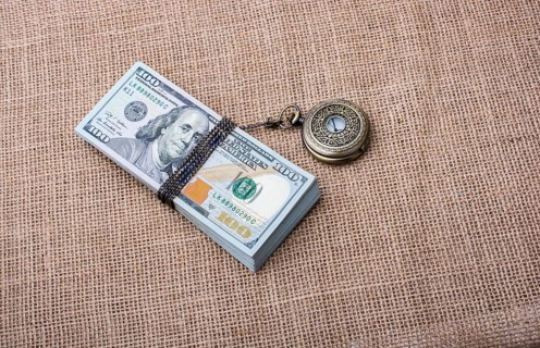 Pocket watch wrapped around banknote bundle of US dollar