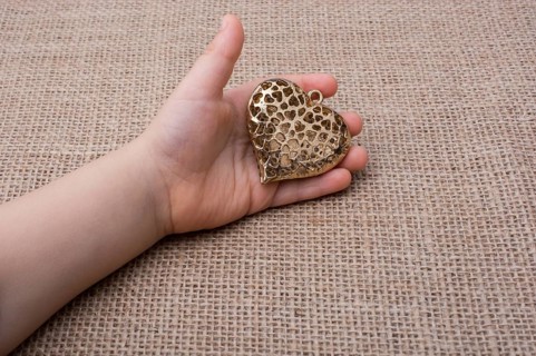Heart shaped gold color metal object in hand