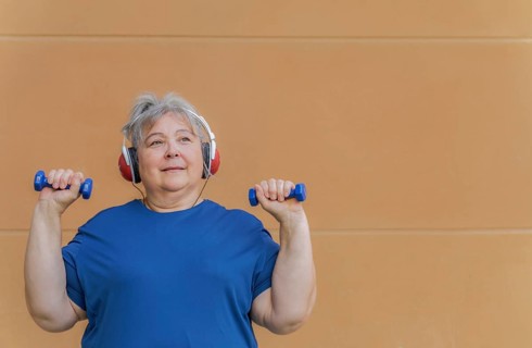 White haired obese older woman exercising with dumbbells and headphones listening to music for weight loss .isolated on orange background and copy space