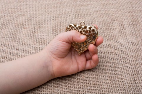 Heart shaped gold color metal object in hand