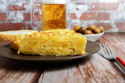 Typical spanish potato omelette freshly made on a wooden table with a fresh pitcher of beer