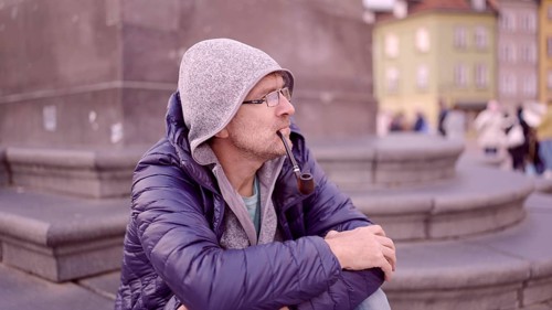 Portrait of adult man with glasses sitting in the hood on square and smoking a tobacco pipe in the Palace Square