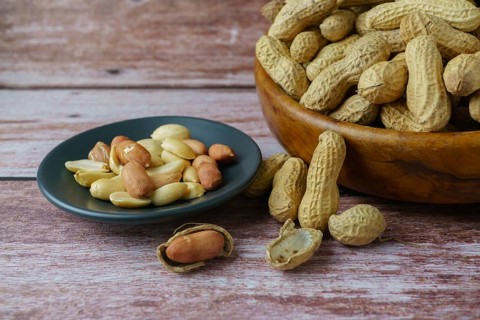 Peanuts in a wooden bowl with peeled peanuts and butter on a spoon