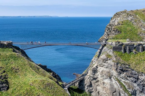 Tourists walk across the new footbridge to the peninsula with the castle ruins of Tintagel Castle