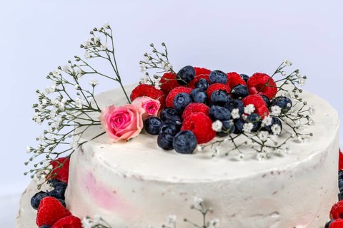 Summery fresh two tier wedding cake decorated with berries and flowers festive cream cake on light background