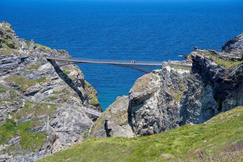 Tourists walk across the new footbridge to the peninsula with the castle ruins of Tintagel Castle