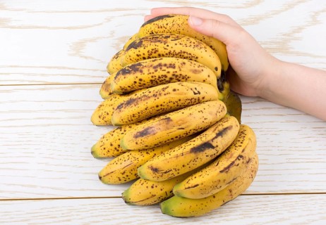 Hand holding bunch of freckled bananas on a wooden texture