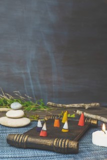 Colorful incense cones burning and smoking on a wooden tray with stacked zen stones